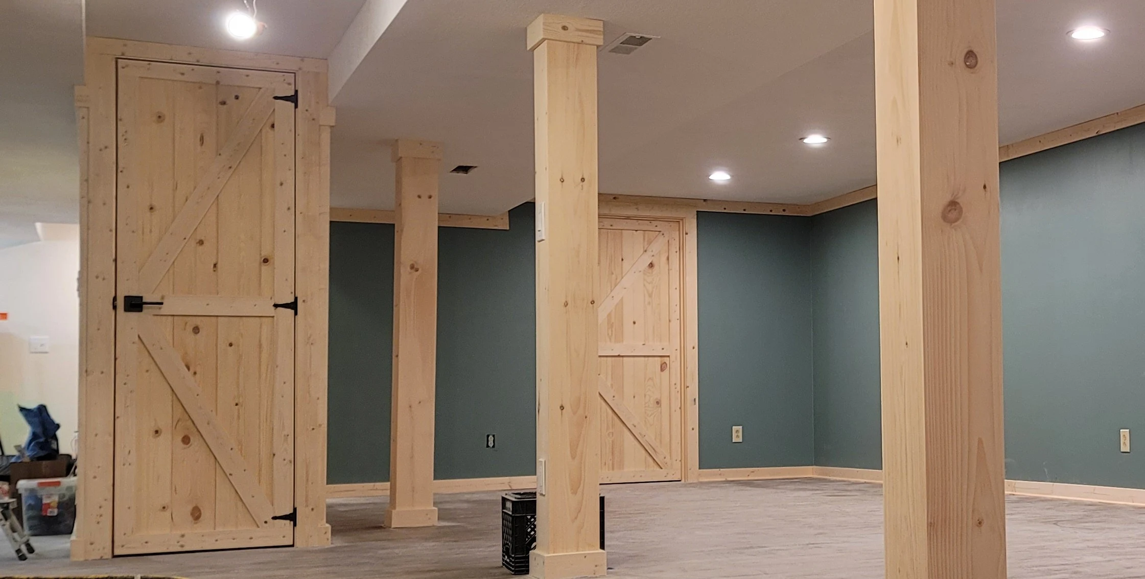 Finished basement room with box-beam columns, barn door, and green accent walls