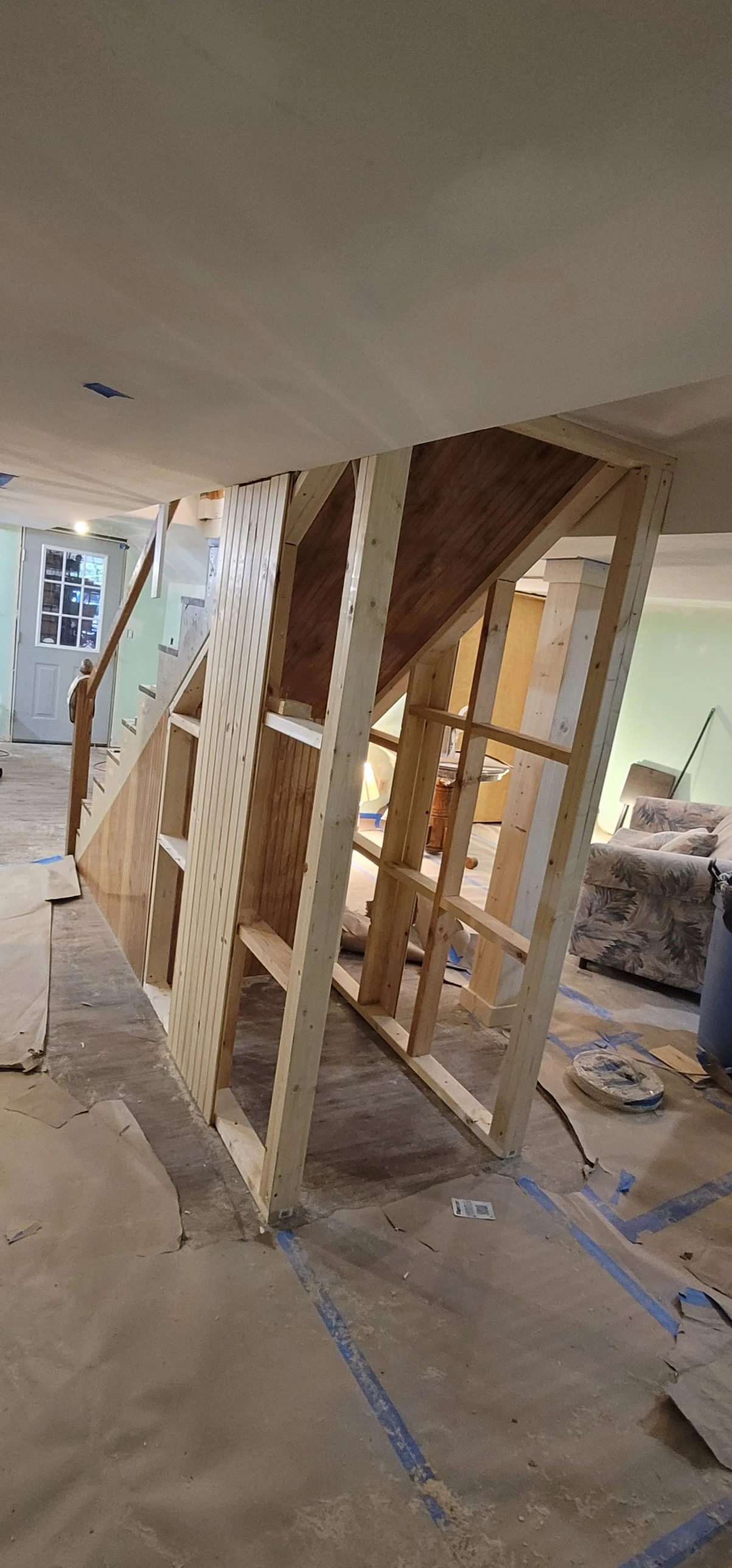 Framed stud wall with partial pine paneling, under-stair storage closet mid-construction
